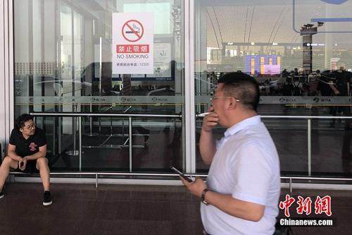 5月25日，一男子在北京首都机场的禁烟标识下吸烟通过。 冷昊阳 摄